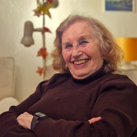 Paula Hilsemer sitzt verschmitzt lachend mit verschränkten Armen auf ihrem Sofa
