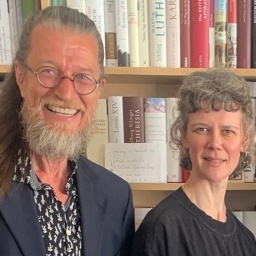 Joachim Dicks und Lisa Kreißler stehen vor einer Bücherwand und lächeln. 