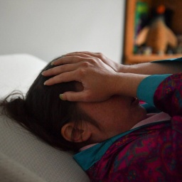 Eine Patientin, die seit 2020 an Long Covid leidet, liegt im Bett und hält die Hände vors Gesicht. 