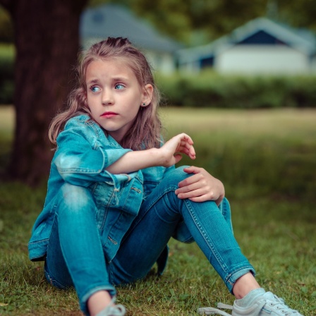 Ein Mädchen sitzt im Gras und guckt sorgenvoll.