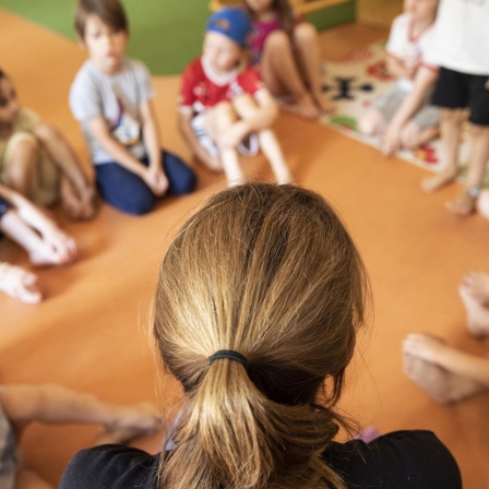 Eine Erzieherin sitzt mit Kinder in der Kita auf dem Boden.