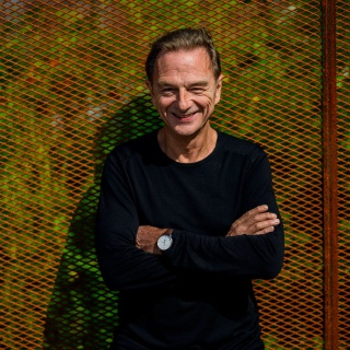 Kabarettist und Autor Fritz Eckenga lehnt mit verschränkten Armen an einem Zaun und lacht in die Kamera