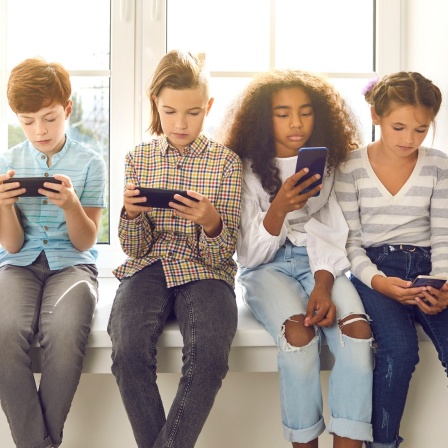 Eine Kindergruppe sitzt auf einer Fensterbank und jeder schaut auf sein Smartphone.