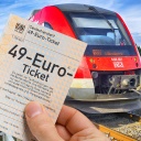Fotomontage: Eine Hand hält ein 49-Euro-Ticket vor einer Regionalbahn (Symbolfoto)