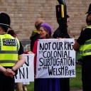 Eine Frau protestiert mit einem Schild gegen den neuen Königs George III. Darauf ist zu lesen: "Nicht unser König". Vor ihr stehen zwei britische Polizisten. 