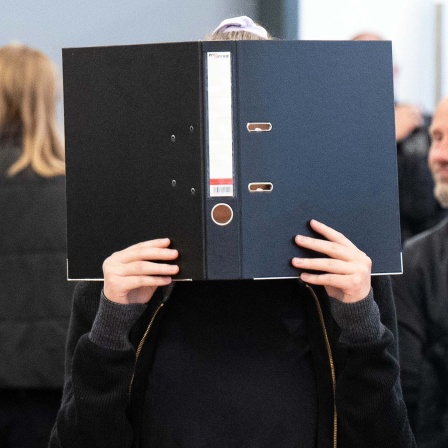 Die Angeklagte Lina E. steht bei der Fortsetzung des Prozesses im Oberlandesgericht (OLG) Dresden im Verhandlungssaal und hält einen Aktenordner vor ihr Gesicht.
