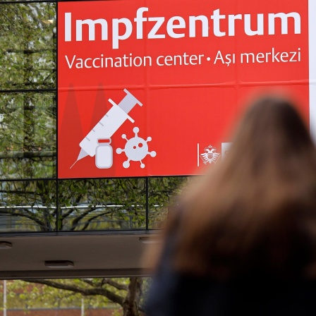 Eine Frau steht vor dem Hinweisbanner für ein Impfzentrum