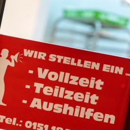 Ein rotes Schild mit der Aufschrift "Wir stellen ein - Vollzeit, Teilzeit, Aushilfen" hängt am Eingang einer Bäckerei in der Innenstadt.