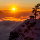 Eine Gruppe von Menschen steht auf einer Bergkuppe vor einem goldenen Sonnenuntergang. 