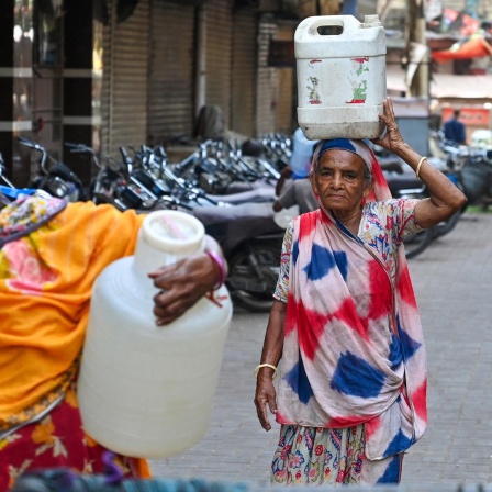 Zwei Frauen in Saris laufen mit schweren Wasserkanistern eine Straße entlang.