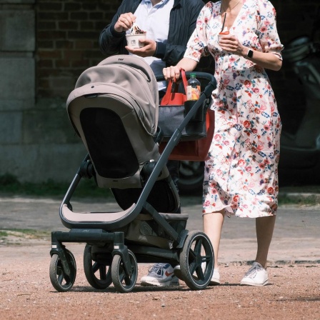 Eine Frau schiebt einen Kinderwagen. Direkt hinter ihr geht ein Mann. 