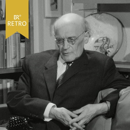 Rudolf-Schmitt-Sulzthal auf einer Couch im Jahr 1967. Im Hintergrund ist auf einer Schale ein Tukan abgebildet.