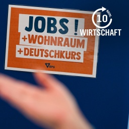 Auf einer Jobmesse für Geflüchtete steht ein Schild mit der Aufschrift Jobs! + Wohnraum + Deutschkurs