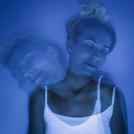 Eine lächelnde Frau mit geschlossenen Augen unter blauem UV-Licht.
