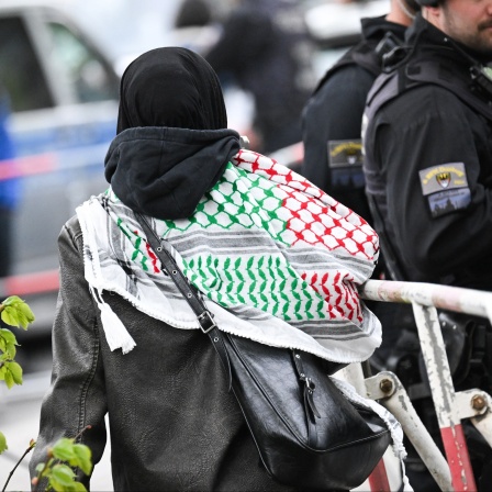 Eine Aktivistin mit Kufiya geht vor der Veranstaltungshalle des Palästina-Kongress 2024 an einer Polizeisperre entlang.