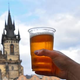 Eine Person hält einen Bierbecher vor der Prager Teynkirche (Foto: imago images / Panthermedia)