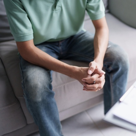 Inszeniertes, ausschnitthaftes Foto einer Therapiesitzung in der sich zwei Personen gegenüber sitzen.