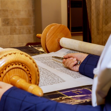 Ein Junge hält einen silbernen Stab, eine Lesehilfe, in der Hand und liest aus der Tora-Schriftrolle.