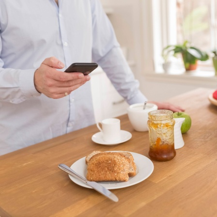 Mann mit Handy am Frühstückstisch
