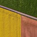 Landwirtschaftliche Felder in grün, gelb und braun sind aus der Vogelperspektive zu sehen, dazwischen führt eine Straße hindurch.