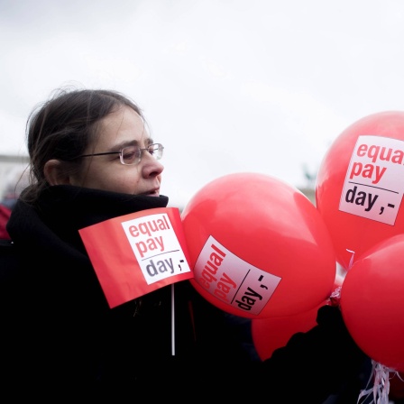 Demonstrantin mit Fahne und Ballon bei einer Kundgebung zum Equal Pay Day