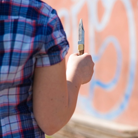 Mädchen steht mit einem Messer in der Hand vor einer Graffitiwand