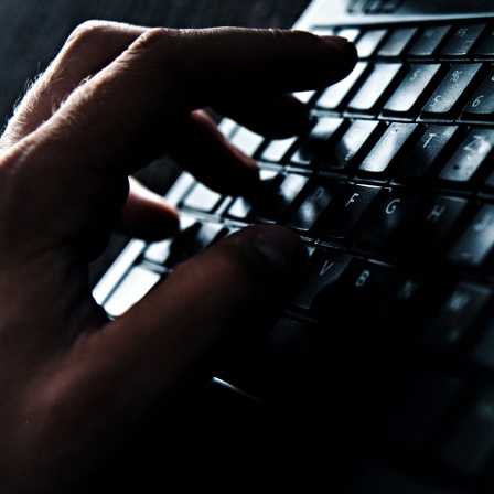 Ein dunkles Foto einer Hand, die über einer schwarzen Tastatur schwebt.