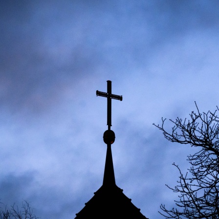 Dunkle Wolken ziehen über das Kreuz auf einer evangelischen Kirche in der Region Hannover hinweg