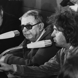 Auf diesem Schwarz-Weiß-Bild sitzen zwei Männer nebeneinander vor Mikrofonen. Der ältere der beiden, Jean-Paul-Sartre, trägt eine dunkle Brille.