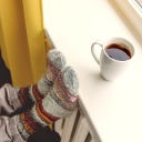 Eine Tasse mit heissem Tee steht auf einer Fensterbank, Füsse in Wollsocken liegen auf der Heizung.