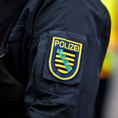 Das Abzeichen der sächsischen Polizei ist auf dem Arm einer Polizeiuniform zu sehen.