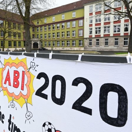 "Abi 2020” steht auf einem selbst gemalten Abi-Plakat, das vor einer Schule aufgehängt ist