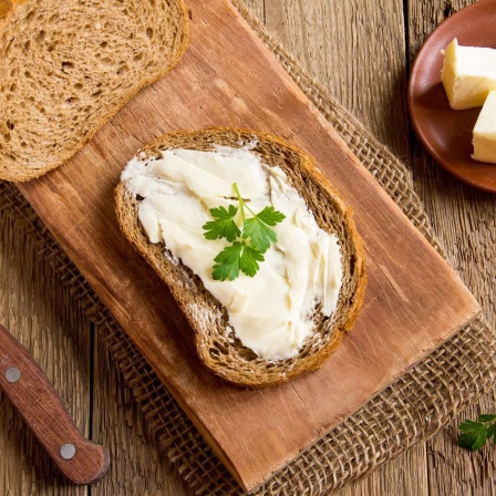 Eine mit Butter bestrichene Scheibe Vollkornbrot liegt auf einem Brett. 