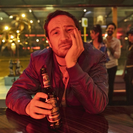 Ein Mann sitzt mit einer Bierflasche in der Hand an einem Kneipentresen.
