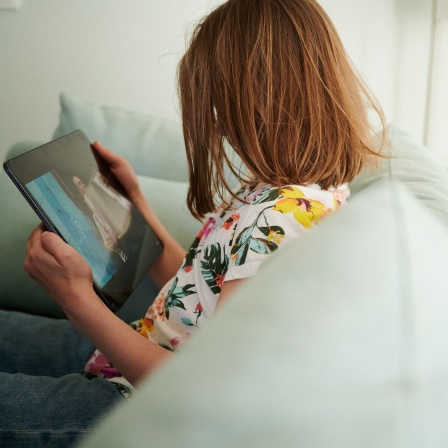 Ein Mädchen sitzt auf der Couch und guckt in das Tablet ihrer Eltern