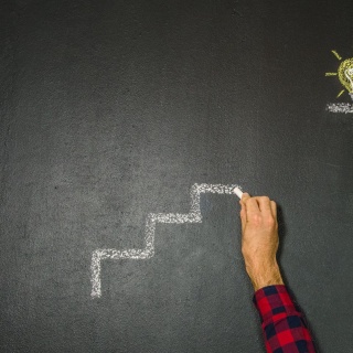 Ein Mann malt mit Kreide eine Treppe, oben ist eine Glühbirne gemalt.