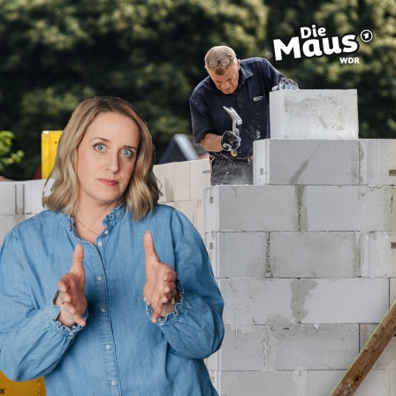 Auf dem Bild ist eine Baustelle zu sehen, auf der ein Bauarbeiter mit Hammer und Handschuhen eine Mauer aus weißen Steinen errichtet, während im Vordergrund eine Frau in einer Jeansbluse mit erklärender Geste steht.