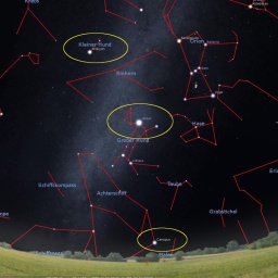 Sternbilder im Himmel. Der Horizont ist dunkelblau, fast schwarz und unten sieht man eine grüne Wiese und Bäume. Die Sternbilder sind durch rote Linien erkennbar. Drei sind gelb umkreist.