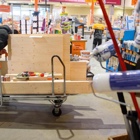 Ein Kunde schiebt in einem Baumarkt einen beladenen Einkaufswagen durch einen Gang.