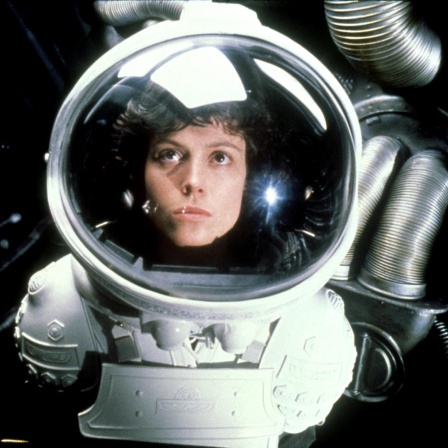 Sigourney Weaver als Officer Ellen Ripley trägt einen Raumanzug und schaut durch das Sichtfenster ihres Helms nach oben.