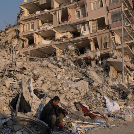 Ein Mann sitzt auf den Trümmern eines eingestürzten Gebäudes.