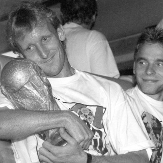 Der deutsche Abwehrspieler Andreas Brehme (l) hält 1990 in Rom den eroberten WM-Pokal im Arm und sein Teamgefährte Thomas Häßler schaut lächelnd zu 
