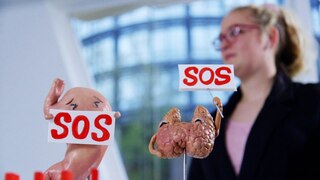 Eine Plastikfigur als Magen und eine Plastikfigur als Schilddrüse halten jeweils ein SOS-Schild hoch.
