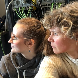 Seitliches Porträt Juliane Bergmann und Lisa Kreißler vor elektrischen Geräten.