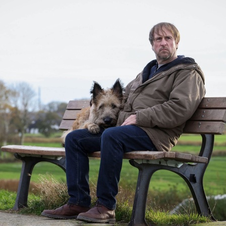 Bjarne Mädel mit einem Hund auf einer Bank