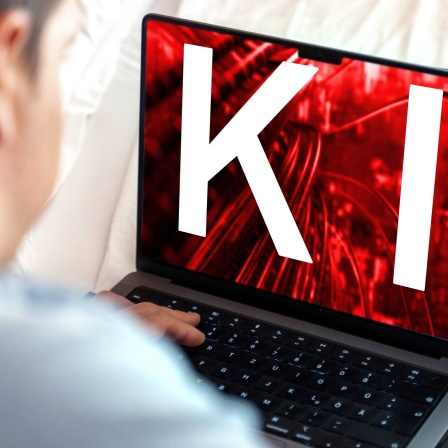 Ein Nutzer arbeitet am Laptop, während der Bildschirm das Kürzel KI und ein digitales Netzwerk in rotem Design zeigt (Bild: IMAGO/Michael Bihlmayer)