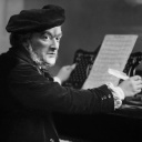 Ein Schwarz-Weiß Portrait des Komponisten Richard Wagner, am Klavier sitzend. Er sitzt mit einer Schreibfeder in der Hand vor seinen Noten.