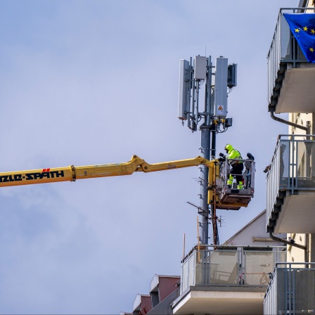 Arbeiter in einem Krankorb montieren auf dem Dach eines Wohnhauses einen Mobilfunkmast.