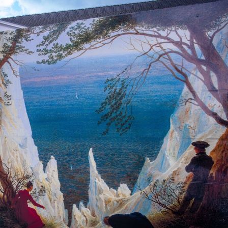 Passanten gehen an großformatigen Kopien von Gemälden von Caspar David Friedrich vor dem Pommerschen Landesmuseum in Greifswald vorbei. (Bild: picture alliance/dpa/Jens Büttner)