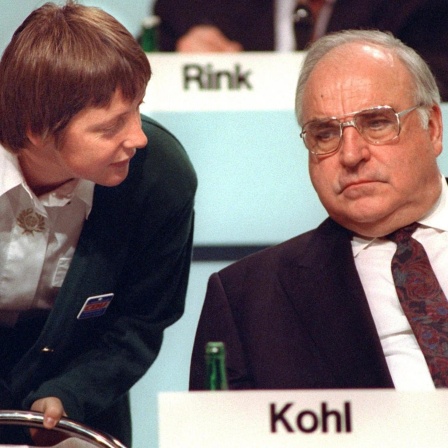 Bundesfrauenministerin Angela Merkel beugt sich am 16.12.1991 während des CDU-Parteitags in Dresden zu ihrem Mentor, Bundeskanzler Kohl, herab. Die Diplom-Physikerin, heute Generalsekretärin der Christdemokraten, wird auf dem CDU-Parteitag vom 9. bis 11.4.2000 in Essen für den Parteivorsitz kandidieren. Die 45-Jährige wäre die erste Frau an der Spitze der Unionspartei - eine Blitzkarriere: Während der Wende engagierte sie sich im "Demokratischen Aufbruch". Nach den ersten freien Volkskammerwahlen war sie stellvertretende Regierungssprecherin der DDR und trat im August 1990 in die Union ein. 1991 holte Kanzler Kohl sie als Ministerin für Frauen und Jugend in sein Kabinett, 1993 wurde sie CDU-Landesvorsitzende in Mecklenburg- Vorpommern, 1994 Bundesumweltministerin. Nach der Niederlage der Christdemokraten bei den Bundestagswahlen 1998 wurde sie zur Generalsekretärin ihrer Partei gewählt.